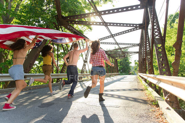 Grupo de amigos correndo na ponte segurando bandeira americana — Fotografia de Stock