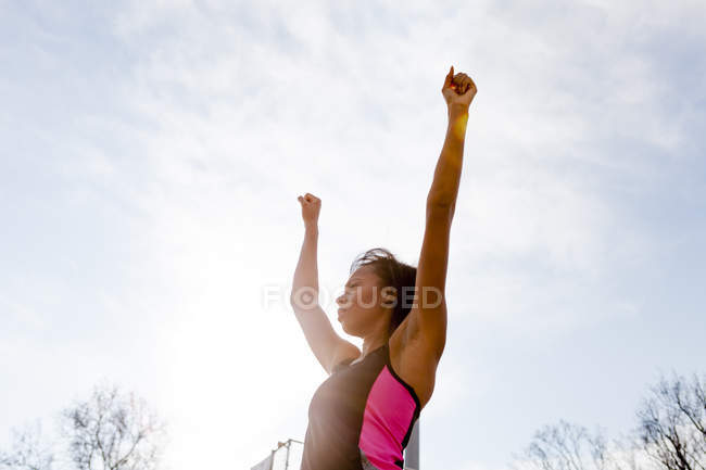Jovem mulher vestindo roupas esportivas, braços levantados, comemorando, visão de baixo ângulo — Fotografia de Stock