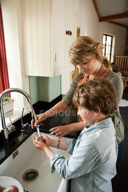 Мати і син миють картоплю в кухонній мисці — стокове фото