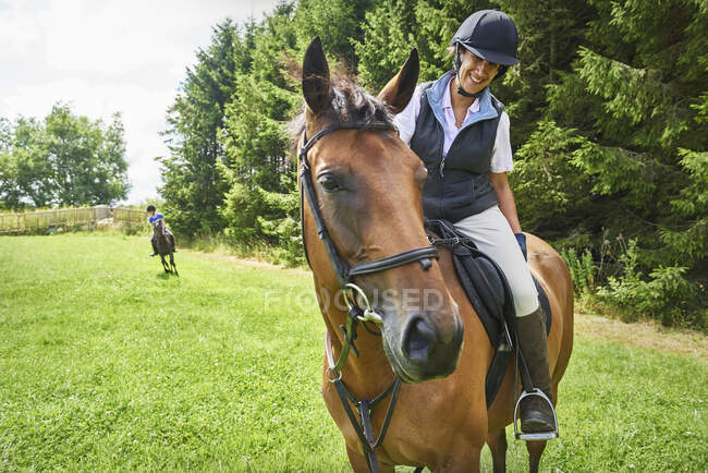 Mature woman on horseback wearing riding hat and boots looking at horse smiling — Stock Photo
