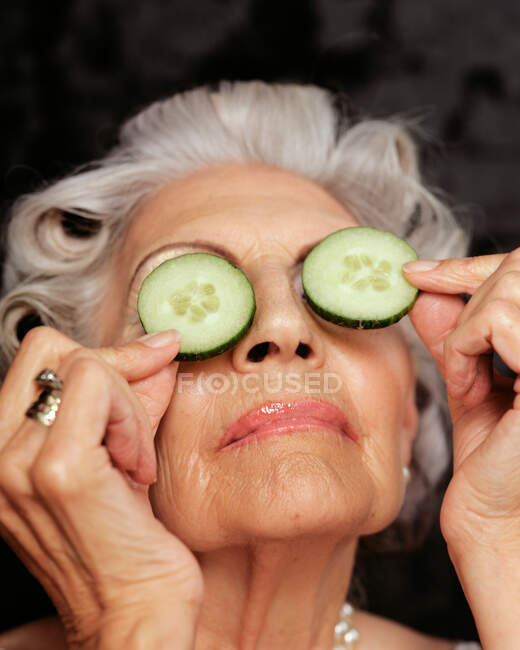 A senior woman holding cucumbers over eyes — Stock Photo