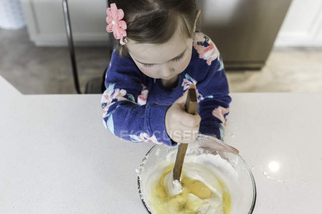 Vista aérea de la chica revolviendo tazón de mezcla en el mostrador de la cocina - foto de stock
