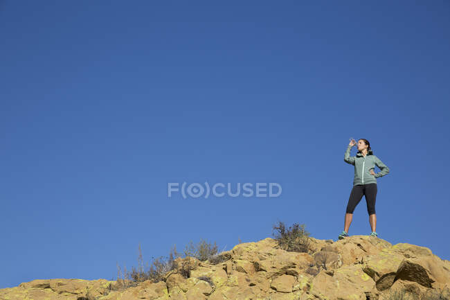 Female runner drinking from water bottle on rugged hill — Stock Photo