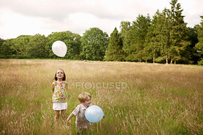 Irmão e irmã em grama alta brincando com balão — Fotografia de Stock