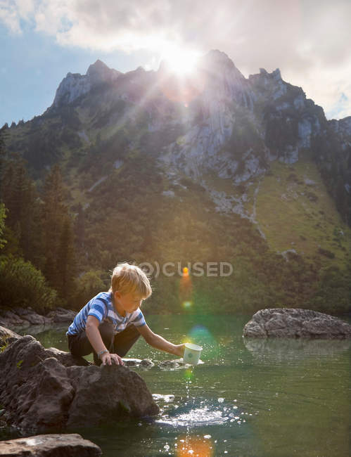 Rapaz mergulhando caneca em lago imóvel — Fotografia de Stock