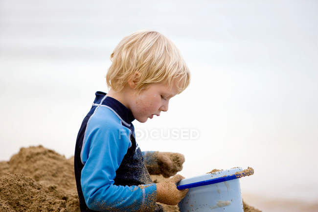 Хлопчик грає з піском на пляжі, фокус на передньому плані — стокове фото