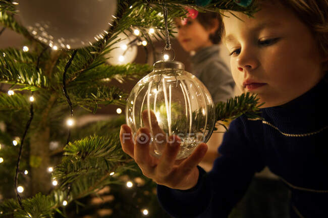 Мальчик украшает елку безделушками дома — стоковое фото