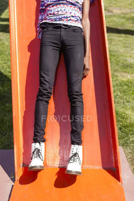 Gambe e stivali bianchi di giovane su scivolo parco giochi arancione — Foto stock