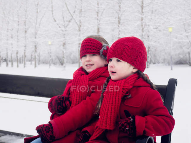 Girls sitting on bench in snow — Stock Photo