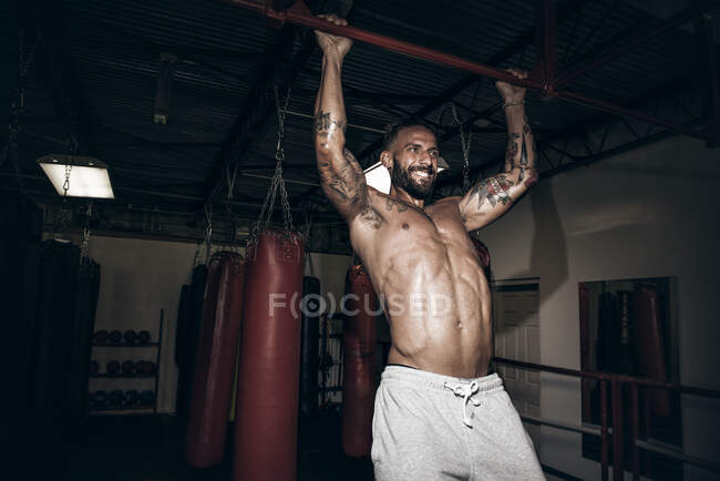 Male boxer doing pull ups with gritted teeth in gym — Stock Photo