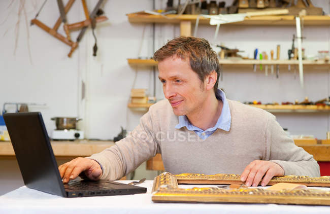Carpenter working on laptop in shop — Stock Photo