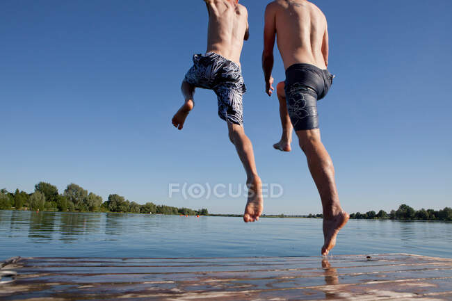 Padre e hijo saltando al lago - foto de stock