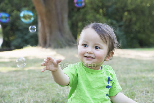 Портрет милого мальчика, тянущегося за пузырьками в парке — стоковое фото