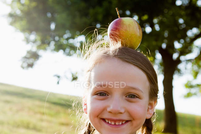 Sonriente chica equilibrando manzana en la cabeza - foto de stock