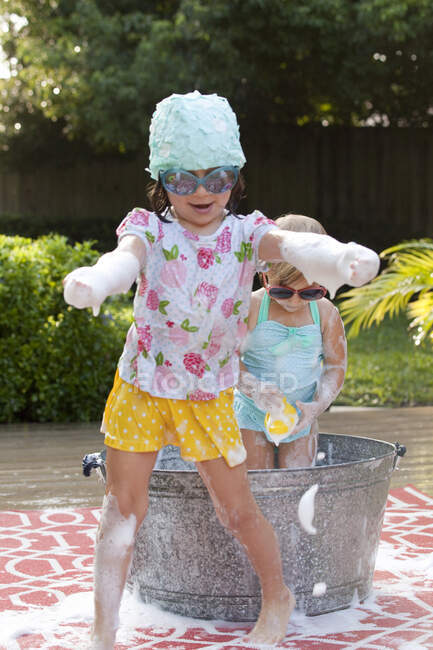 Girl and toddler sister playing in bubble bath in garden — Stock Photo