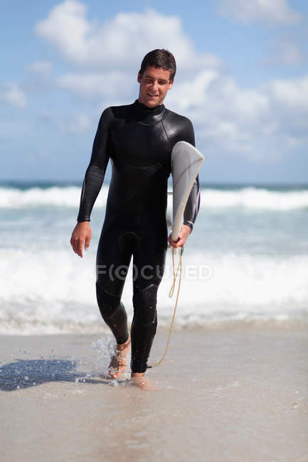Teenage surfer carrying board on beach — Stock Photo