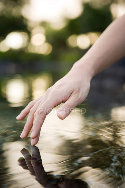 Mão feminina tocando superfície da água — Fotografia de Stock