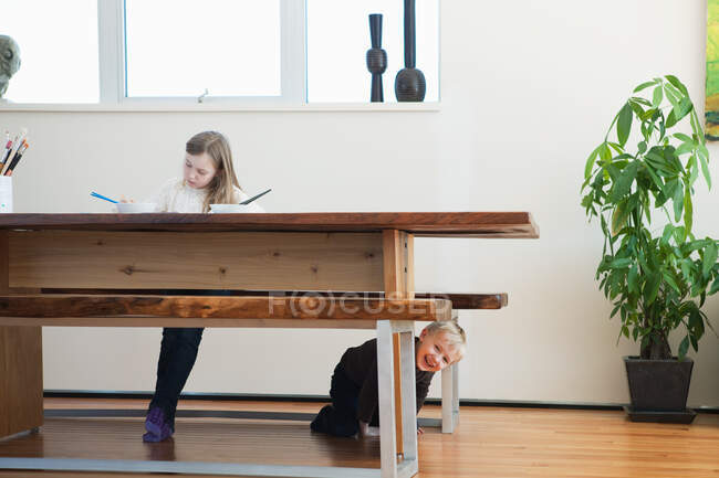 Девушка рисует, брат под столом — стоковое фото