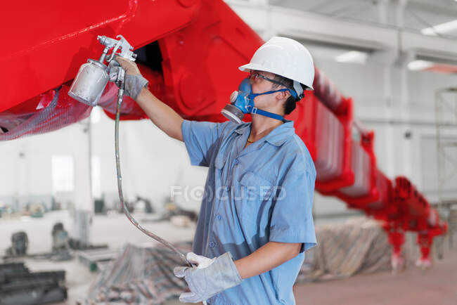 Trabajador masculino pulverización pintura un brazo de grúa rojo en taller de fábrica, China - foto de stock