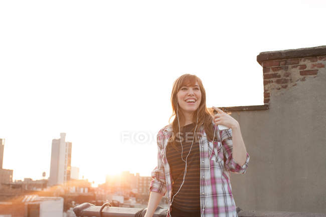 Young woman listening to music on city rooftop — Stock Photo
