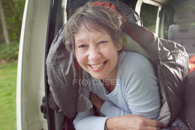 Portrait of senior woman inside sleeping bag, in open camper van — Stock Photo