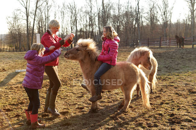 Giovane ragazza cavalcando pony, madre e sorella in piedi accanto a loro — Foto stock