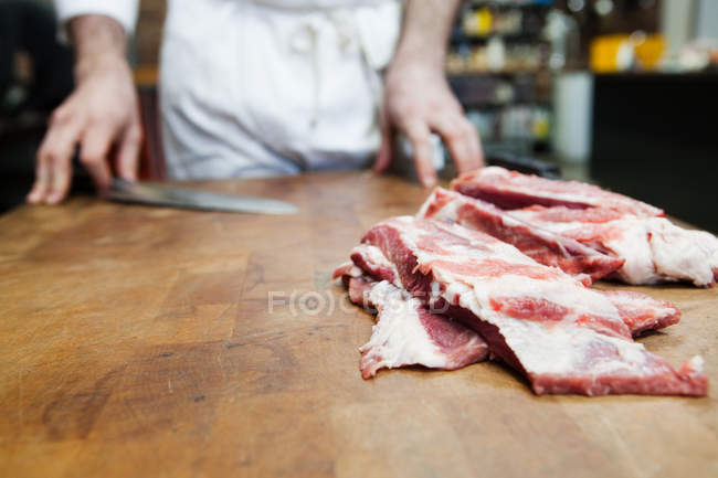 Крупным планом видны сырые свиные ребра на деревянном столе, мясник стоит позади — стоковое фото