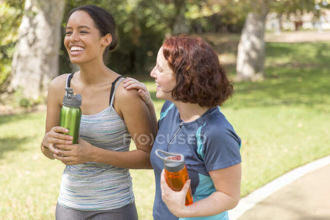 Vista de ángulo alto de mujeres jóvenes caminando usando ropa deportiva llevando botellas de agua sonriendo - foto de stock