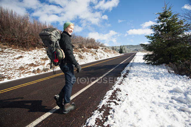 Senderismo masculino joven en carretera rural en el paisaje cubierto de nieve, Ashland, Oregon, EE.UU. - foto de stock