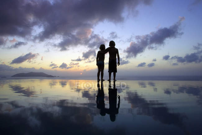 Вид ззаду дітей, що стоять на пляжі на заході сонця — стокове фото