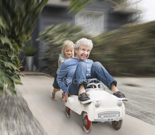 Neto empurrando avó em seu carro de brinquedo — Fotografia de Stock