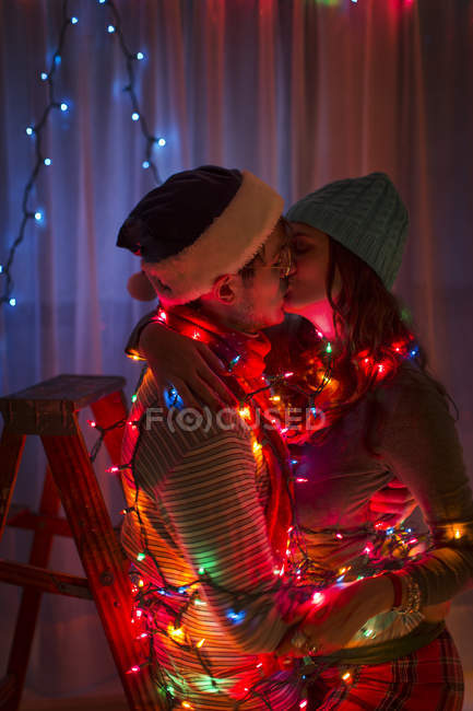 Young couple wrapped in fairy lights at christmas — Stock Photo