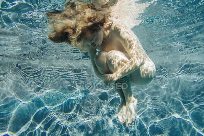 Low angle view of young woman in swimming pool, hugging knees, head down eyes closed — Stock Photo