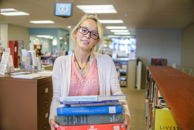 Retrato de jovem bibliotecária carregando pilha de livros — Fotografia de Stock