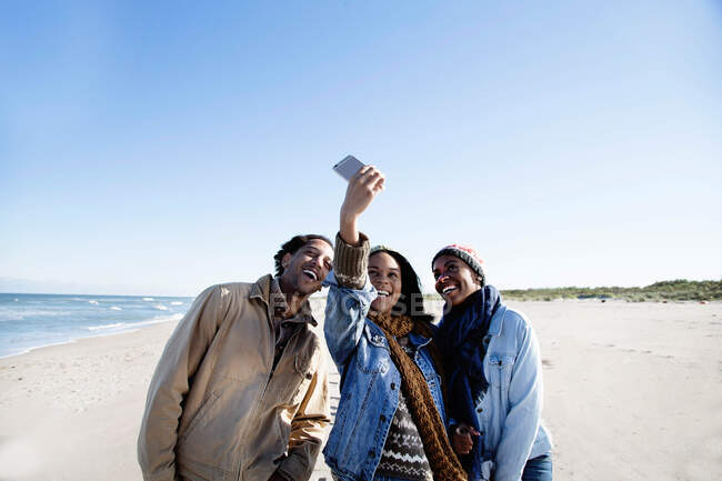 Три друга на пляже, делают автопортрет, используют смартфон — стоковое фото