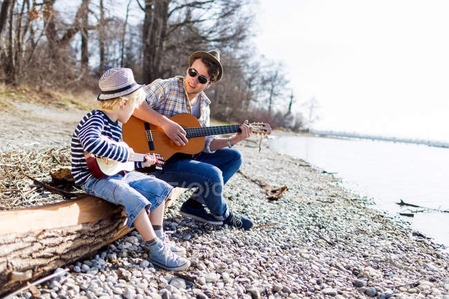 Padre e hijo tocando guitarras por arroyo - foto de stock