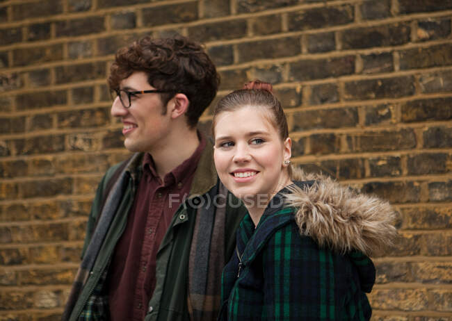 Jeune couple par mur de briques, souriant — Photo de stock