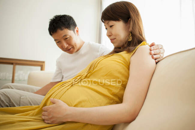 Homme regardant l'estomac de la femme enceinte sur le canapé — Photo de stock
