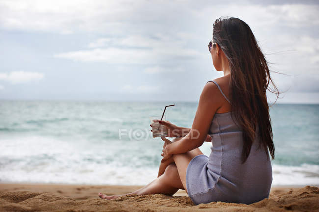 Mujer bebiendo en la playa de arena - foto de stock