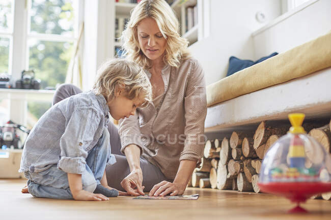 Мати і син сидять на підлозі, роблячи загадку разом — стокове фото