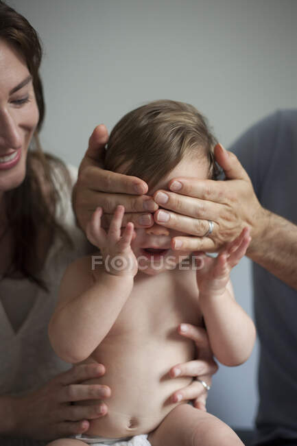Madre y padre jugando a echar un vistazo a un boo con el niño - foto de stock