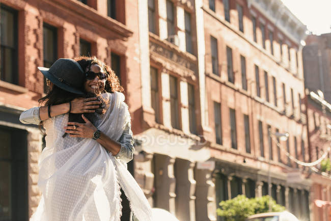 Two mid adult female friends hugging on city street — Stock Photo