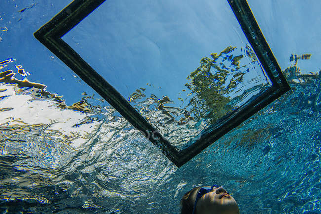 Adolescente chica bajo el agua, mirando a través del marco en la superficie del agua - foto de stock