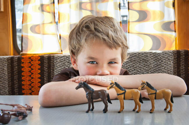 Boy playing with toy plastic horse in caravan — Stock Photo