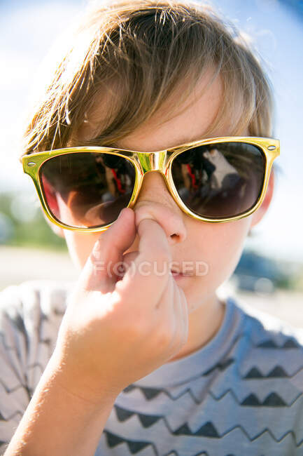 Retrato de niño con gafas de sol doradas que se rascan la nariz - foto de stock