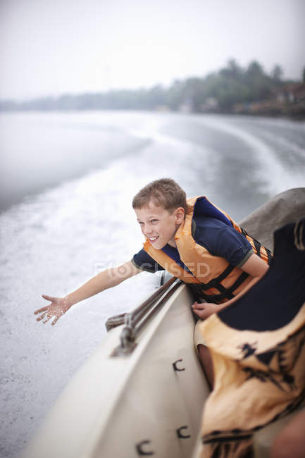 Teenage boy reaching to water from boat — Stock Photo