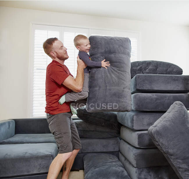 Father and son stacking cushions in living room — Stock Photo