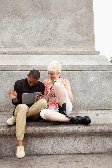 Две молодые женщины сидят на ступеньках с цифровым планшетом — стоковое фото