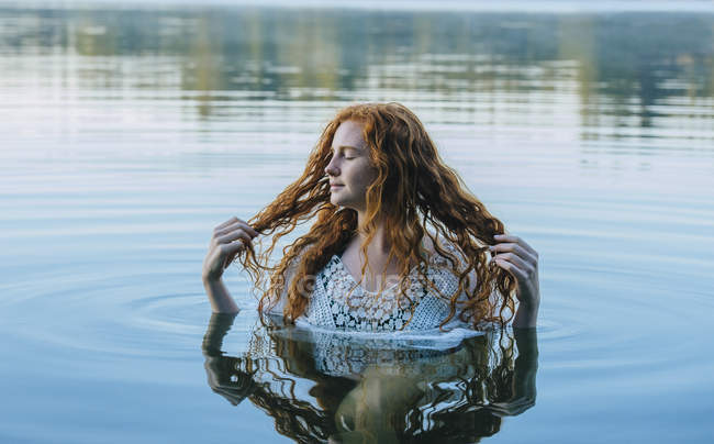 Tête et épaules de belle jeune femme aux longs cheveux roux dans le lac — Photo de stock