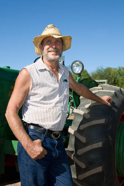 Fermier âgé appuyé contre tracteur, souriant — Photo de stock